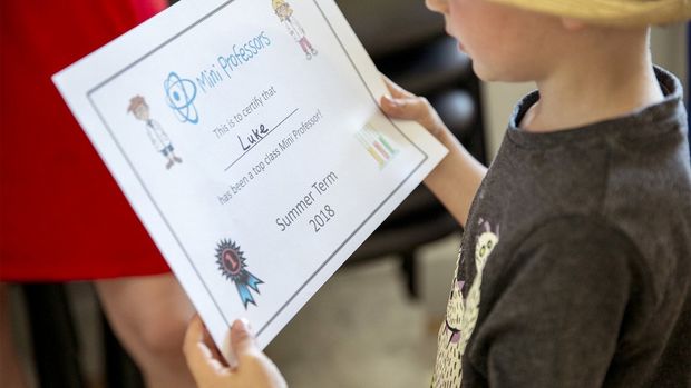 A child holds a Mini Professors certificate with his name on.