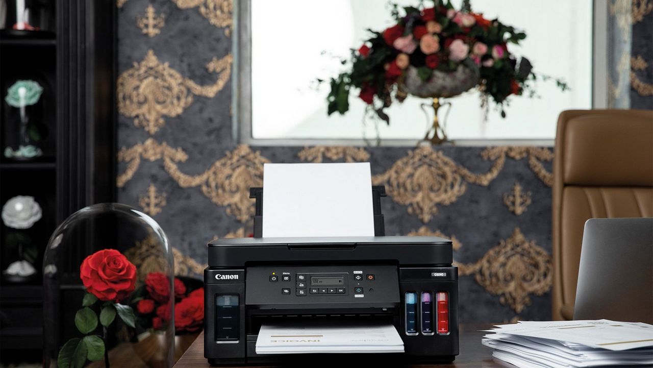 A desk with a Canon PIXMA G6040 and papers on top, next to a glass dome housing for a red rose. 