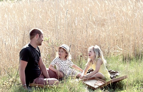 A man and two children sit in a sunny field enjoying a picnic. Photo by Hannah Clark on a Canon EOS 250D.