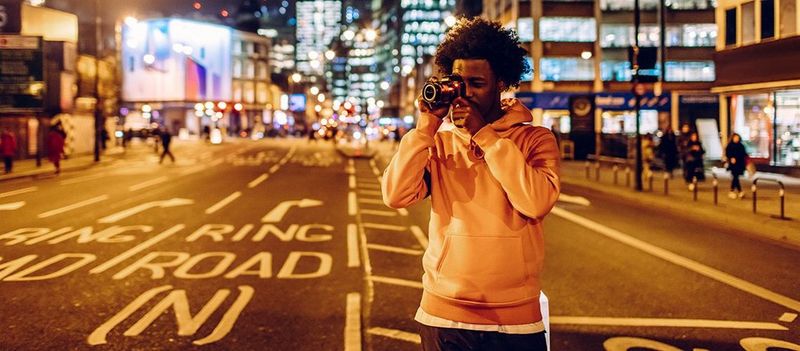 Мужчина стоит возле дороги под мостом в центре города и делает снимок на камеру Canon.