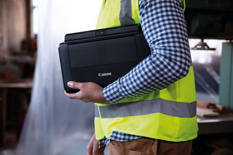 A man in a high-vis jacket carries a PIXMA TR150 under his arm.