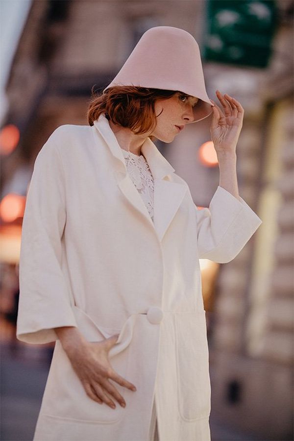 A bride wears a white coat and hat in a city. Photo by Félicia Sisco with a Canon RF 85mm F1.2L USM lens.