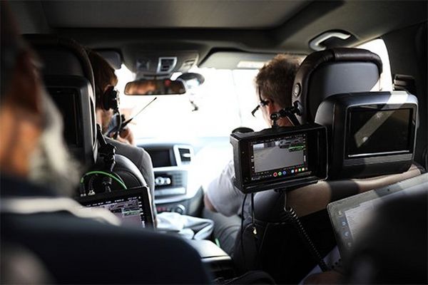 A film crew in the camera car watch footage on monitors.