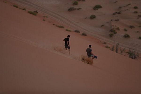 Cameramen run down the side of a high, steep sand dune.