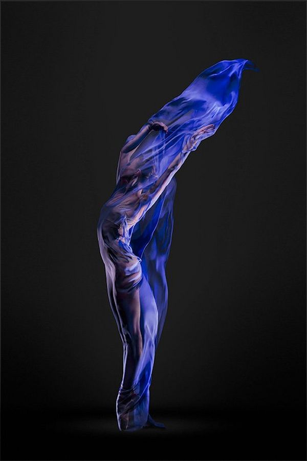 A ballet dancer completely shrouded in blue silks forms a sinuous S-shape like a living flame.