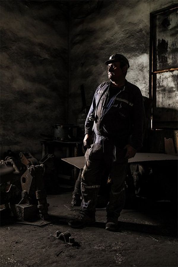 Environental portrait of a miner in a decaying, dust-covered industrial setting.