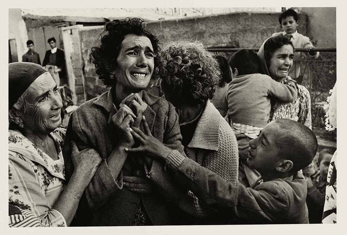 A grieving Turkish woman is comforted by others and clutches her hands to her chest as she mourns her husband, a victim of the Cyprus Civil War.