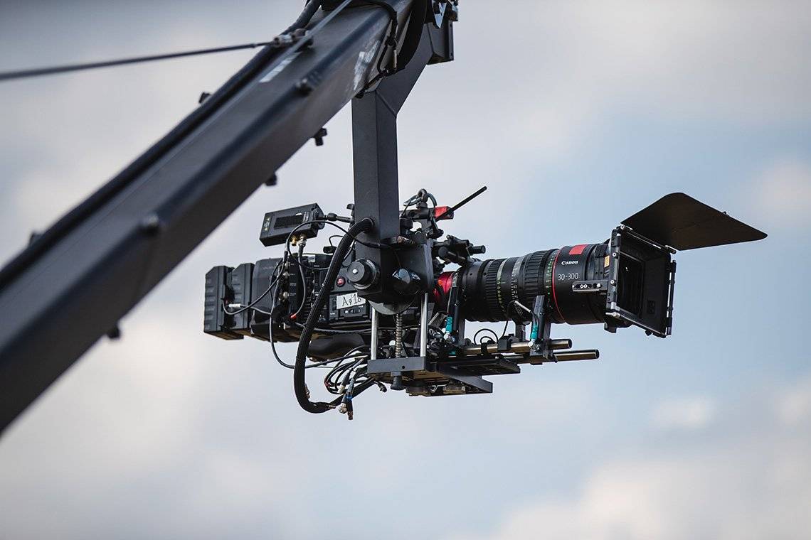 A Canon EOS C700 FF in front of a blue sky hanging from a camera crane.
