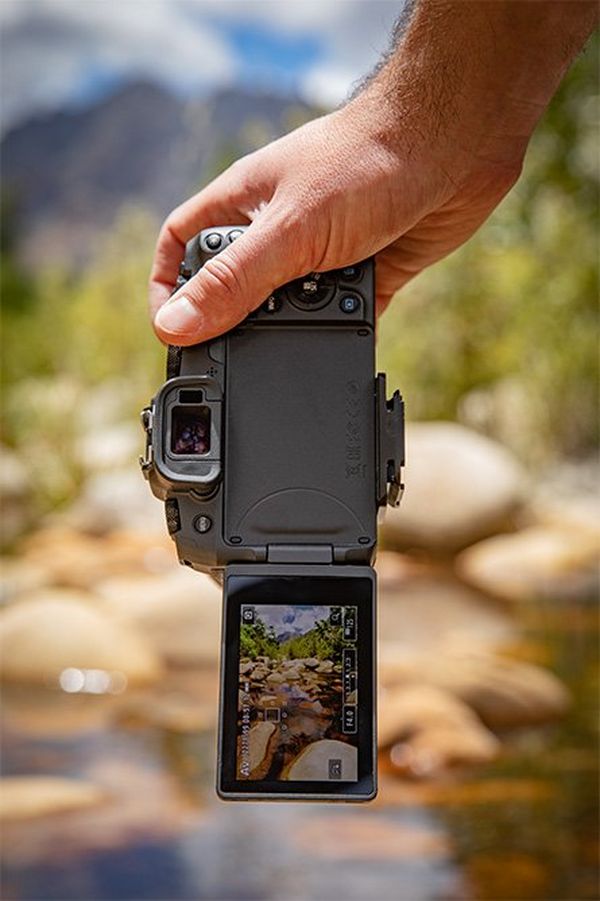 A man holds a Canon EOS RP by a stream.