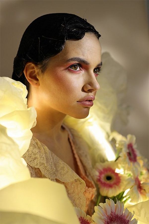 A luminous ring hangs around a white models’ neck, who’s holding flowers and looking pensively into the distance.