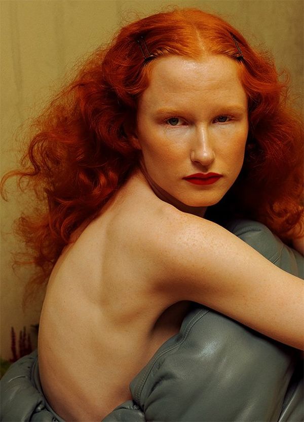 Red-haired model Maisie looks straight at the camera over her bare shoulder.