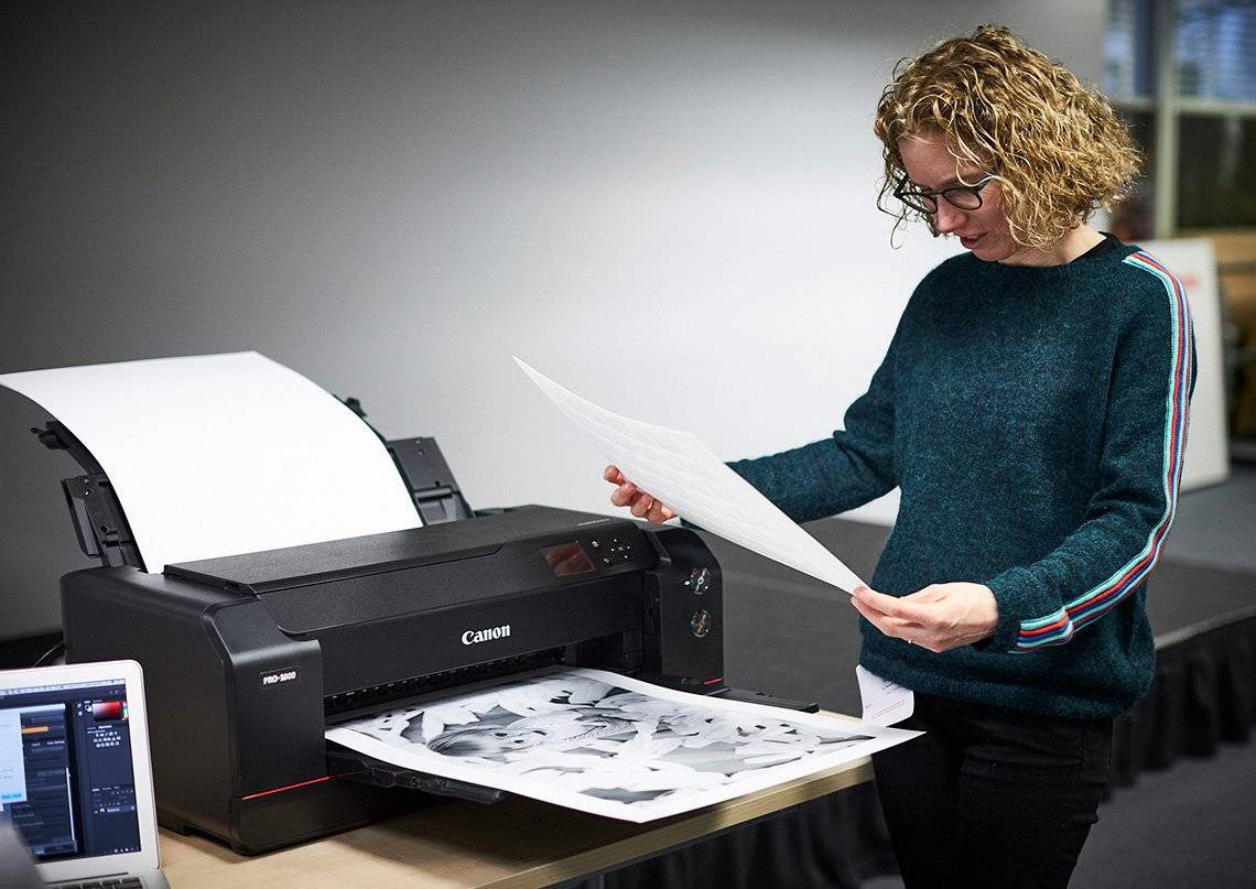 Helen Bartlett stands next to a Canon imagePROGRAF PRO-1000 printer looking at an A2 black and white photo print.