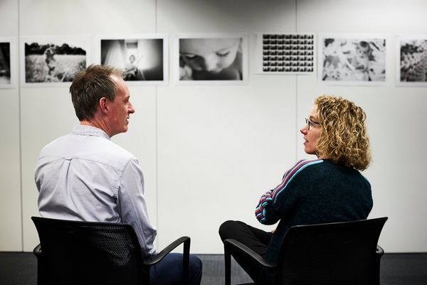 Jay Sinclair and Helen Bartlett sit discussing a set of prints of Helen's photographs displayed on a wall. 