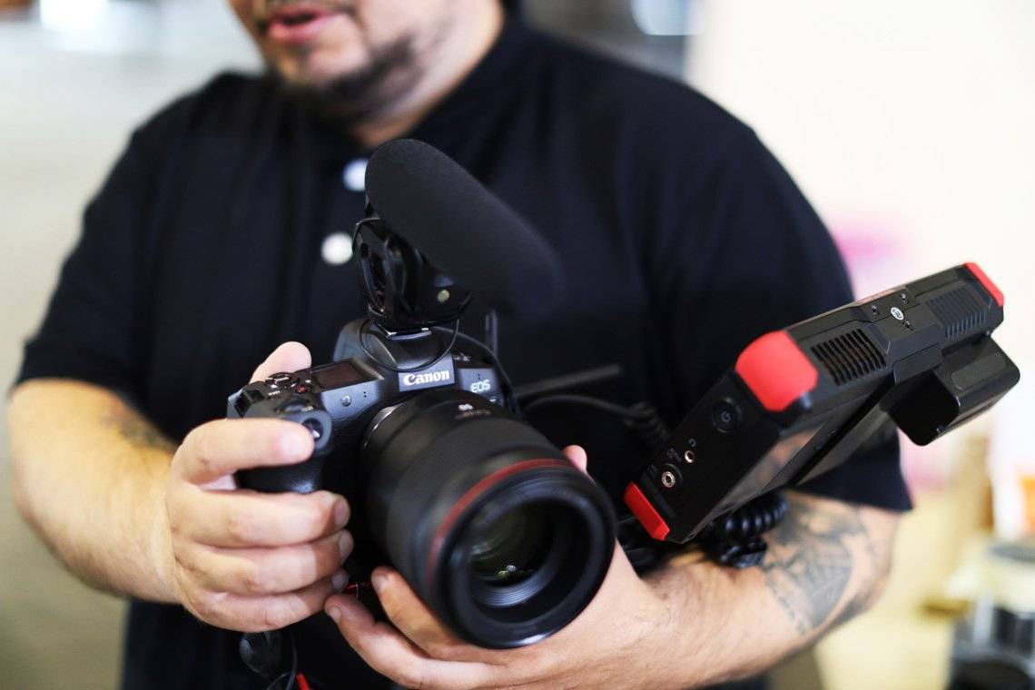 Filmmaker Nicolai Brix, seen out-of-focus from the chin down, holds a Canon EOS R with a microphone attached to the flash shoe at its top and an external display mounted at the side.
