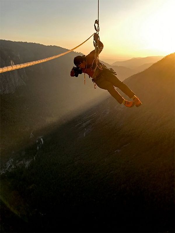 Cinematographer Jimmy Chin dangles in mid air as he films, with the hills of Yosemite National Park lit by the sunset behind him.