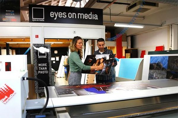 Ilvy Njiokiktjien lifts an exhibition print with a man at Eyes on Media printers.