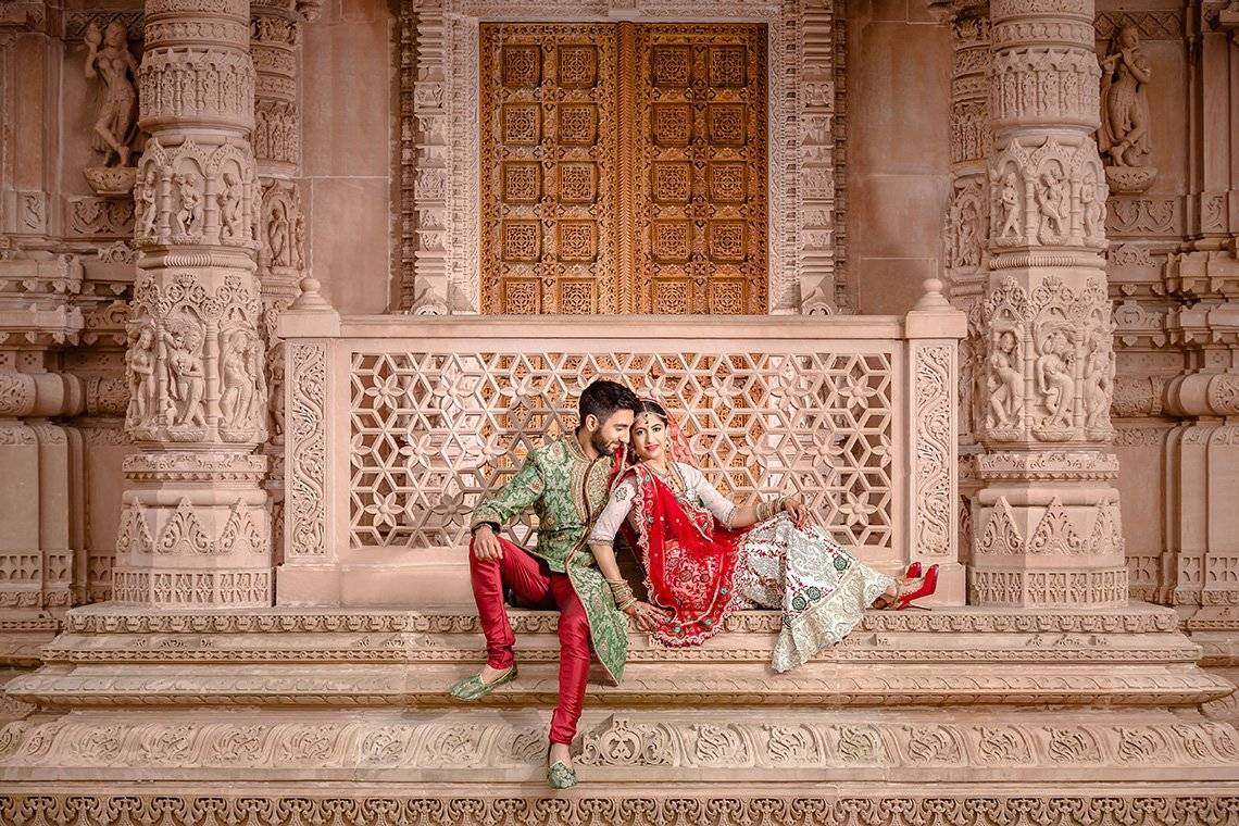 A newlywed couple sit outside the doors of a Hindu temple. Taken by wedding photographer Sanjay Jogia.