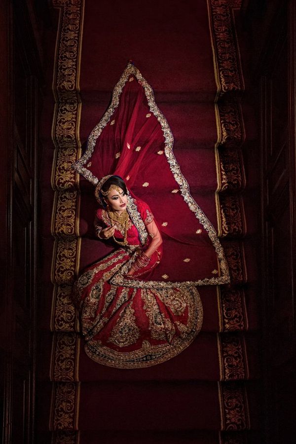 A bride sits on a red staircase, with her red veil laid out on the steps behind her. Taken by wedding photographer Sanjay Jogia.