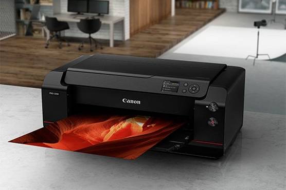 A Canon imagePROGRAF PRO-1000 A2 desktop printer on a marble-effect surface with a colourful red and orange print being output.