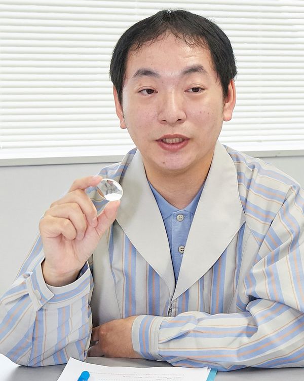 Canon Optical Design specialist Kenji Shinohara holds a UD aspherical lens between thumb and forefinger.