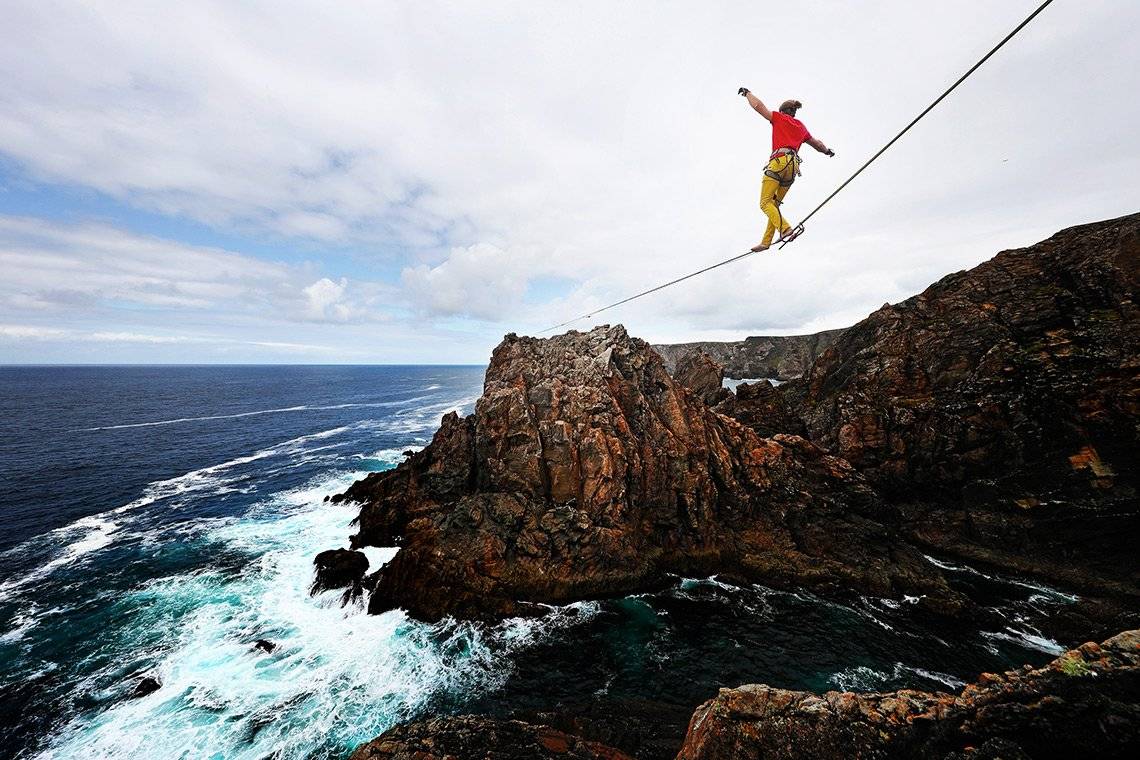 A man balances on a slackline suspended between two cliffs over the sea in Ireland. 