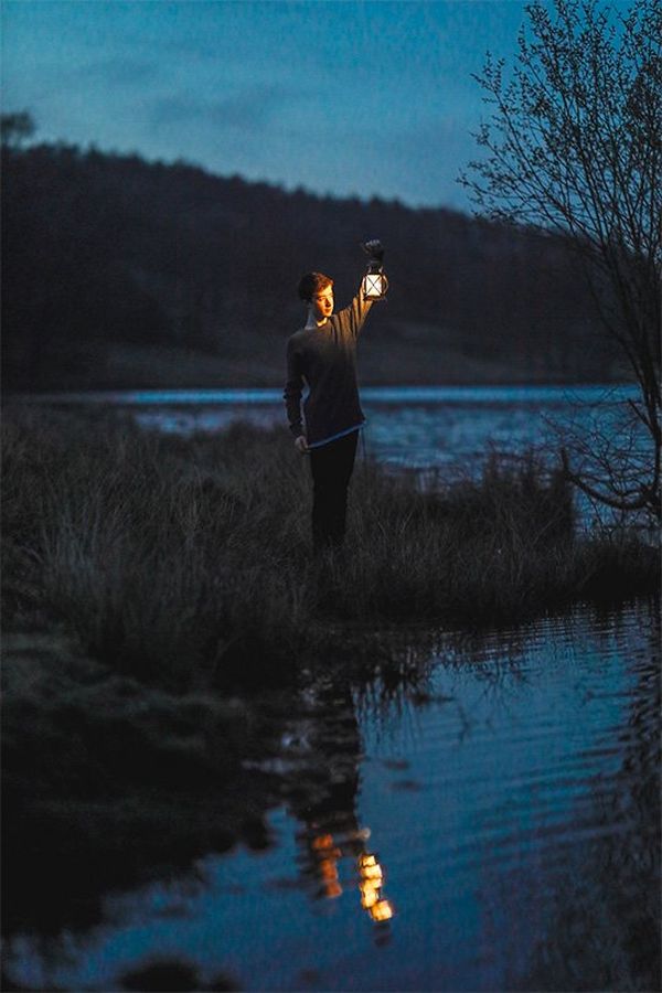A boy holds a lantern by a lake at dusk. Photo by Rosie Hardy with a Canon RF 85mm F1.2L USM lens.