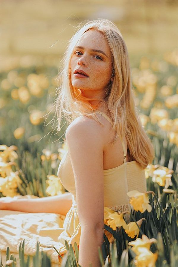 A blonde woman in a yellow dress sits in a sunny field full of daffodils. Photo by Rosie Hardy with a Canon RF 85mm F1.2L USM lens.
