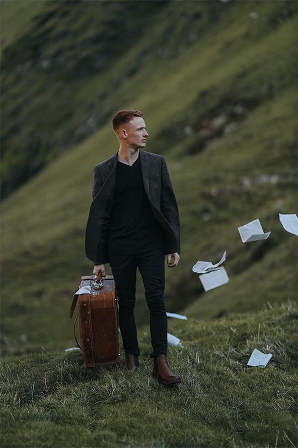 A young man carries a suitcase up a hill, papers flying out on the grass behind him. Photo by Rosie Hardy with a Canon RF 85mm F1.2L USM lens.