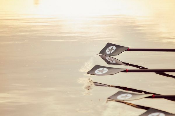 Oar blades are caught mid-stroke, hovering above the water. 