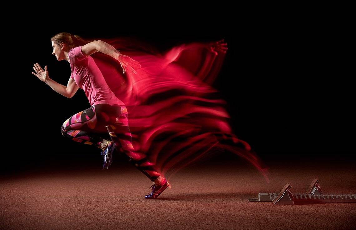 Paralympic runner Libby Clegg runs off her blocks, a trail of pink light visible behind her, giving the illusion of speed.