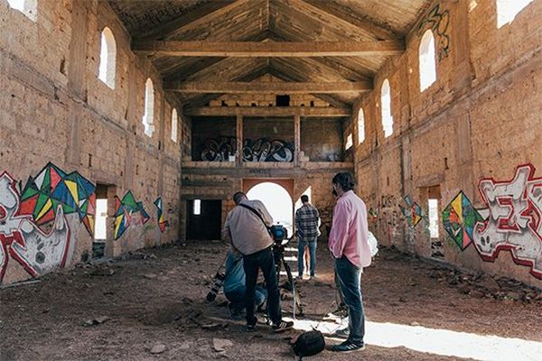 Hans von Sonntag and film crew at work inside a deserted chapel, with glaring light streaming in through the open windows and doorways.