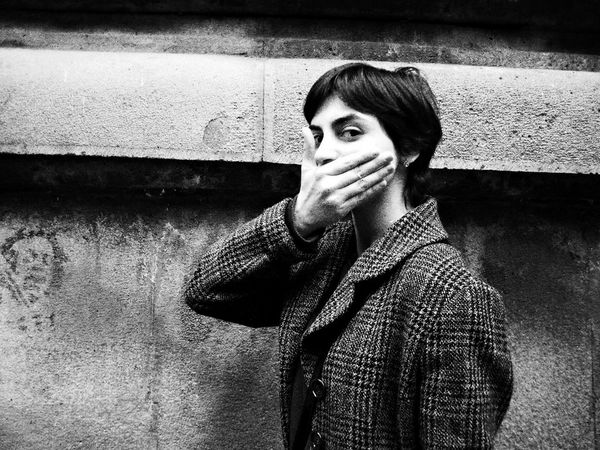A black-and-white shot of a young woman with a wearing a tweed jacket, covering her mouth with her hand. 