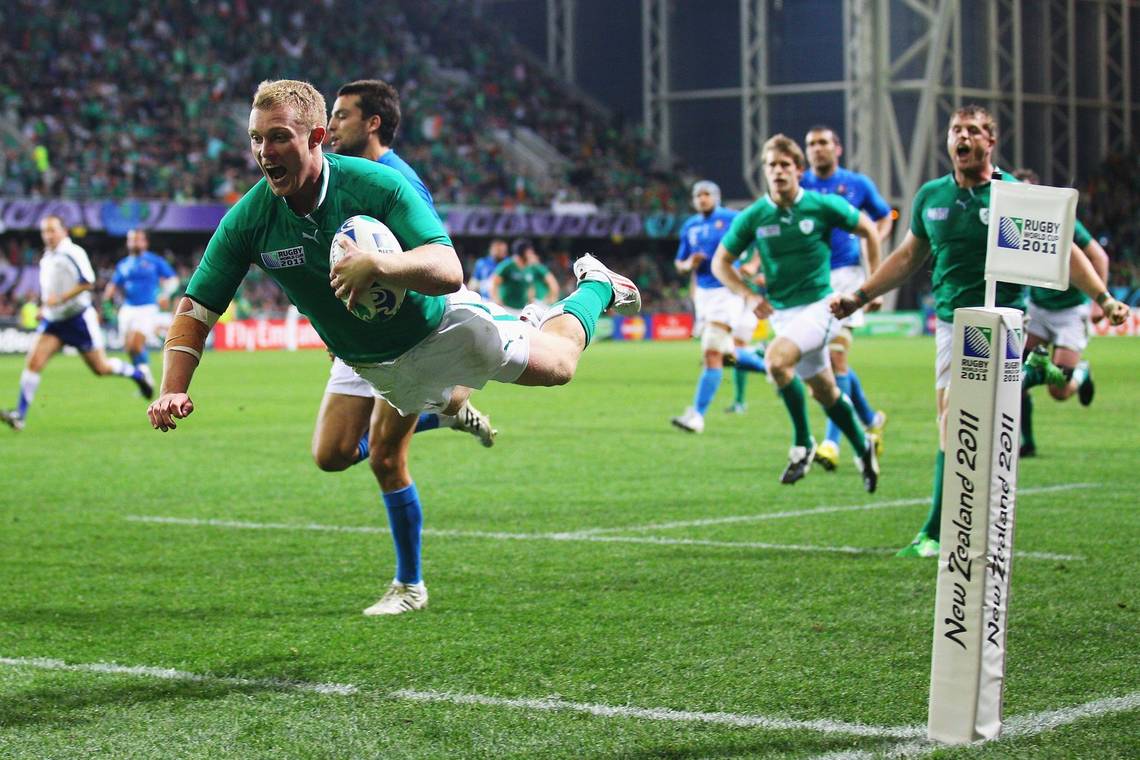 Ireland rugby player Keith Earls jumps over the line to score a try, his teammates looking on.