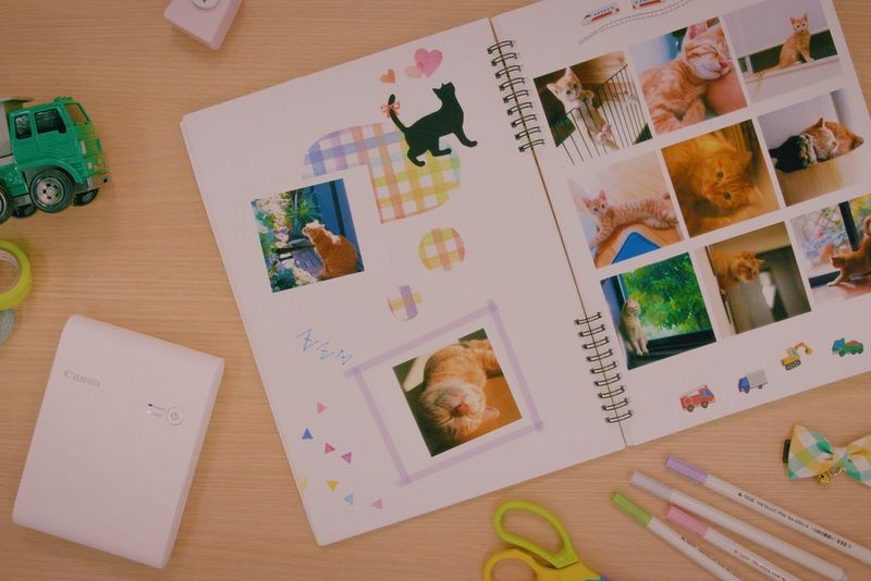 The open pages of a scrapbook showing pictures of cats next to a Canon compact printer.