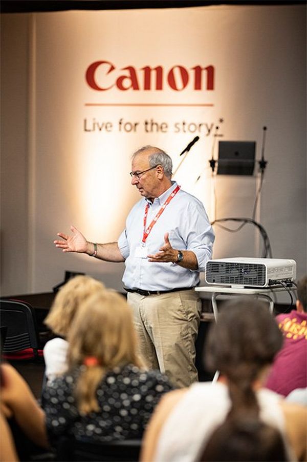 Francis Kohn stands on a Canon-branded stage, speaking to an audience.