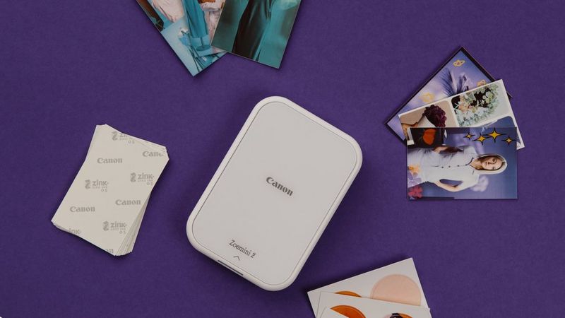 Pearl white Canon Zoemini 2 on a purple table surrounded by printed stickers and ZINK paper.