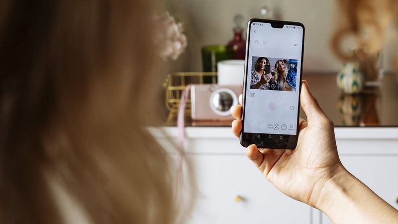 Rose gold Canon Zoemini S2 in the background taking picture remotely of two women with the usage of Mini Print app on the phone one of them is holding in her hand.