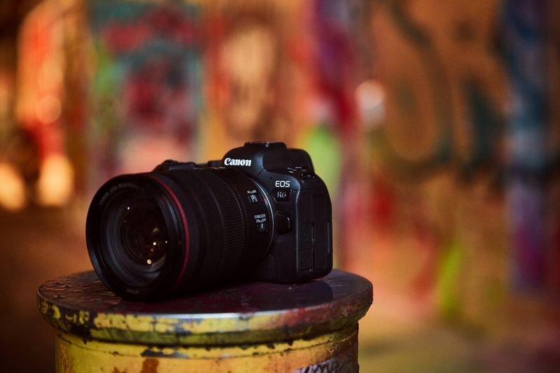 A Canon EOS R6 sits on the lid of a container splattered with colourful paint.