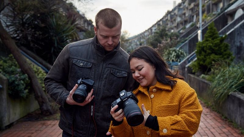 Two people standing next to one another, both holding Canon cameras,  one showing the other something on their Canon camera.