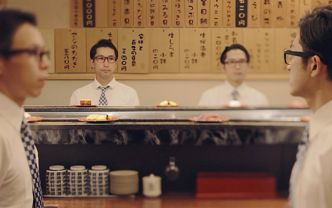 Japanese businessmen sitting in a kaiten-zushi watching sushi plates rotate on a conveyor belt.