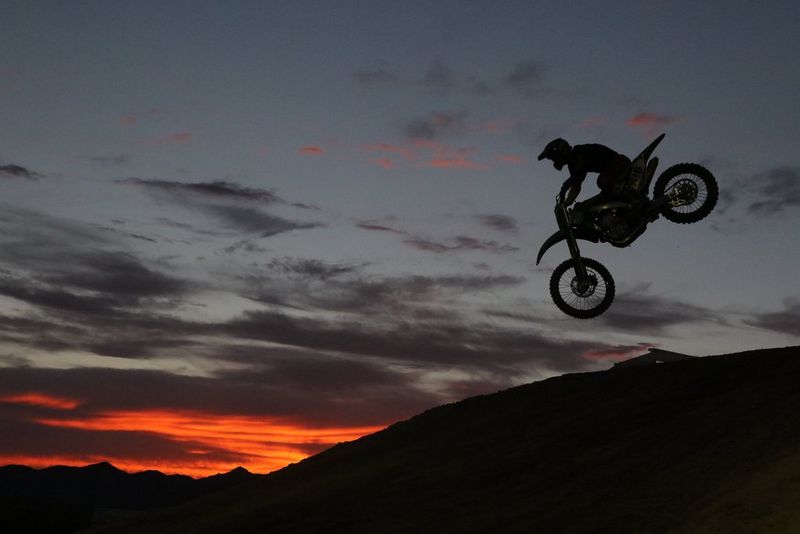 A figure jumping on a dirt bike over a hill, silhouetted against the dusk sky.