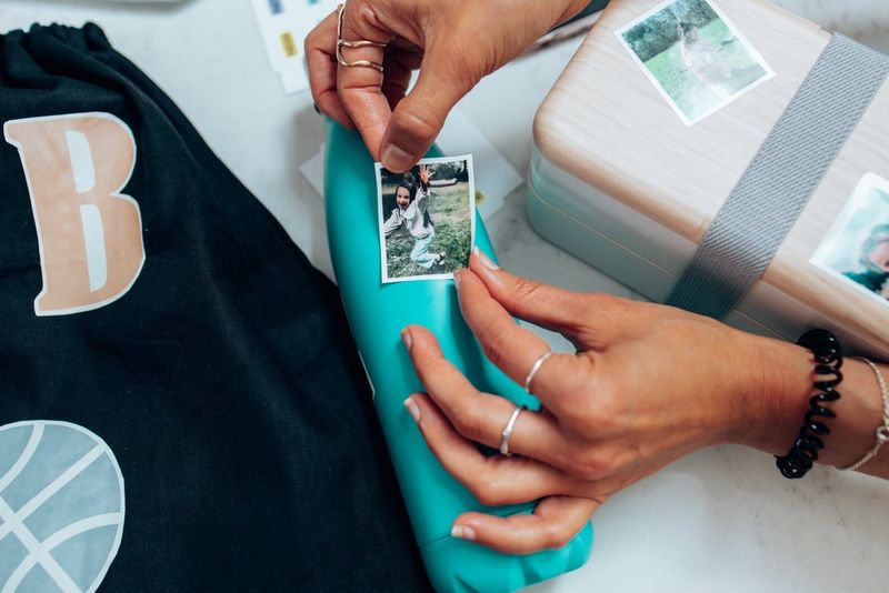 A pair of hands can be seen carefully attaching a sticker with a photograph of a young girl on it to a green water bottle.