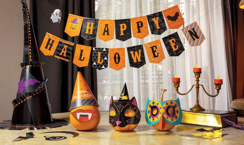 A range of papercraft Halloween masks arranged on a table underneath a 'Happy Halloween' banner.