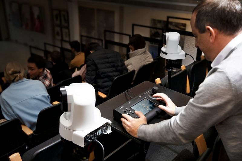 An operator using the Canon RC-IP100 remote camera controller, with two Canon PTZ cameras either side of the table at the back of an auditorium.
