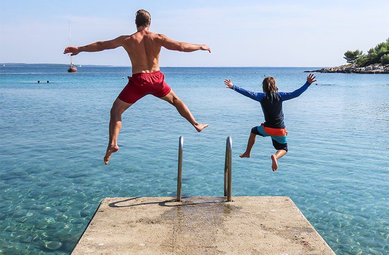dad and son jumping into the ocean