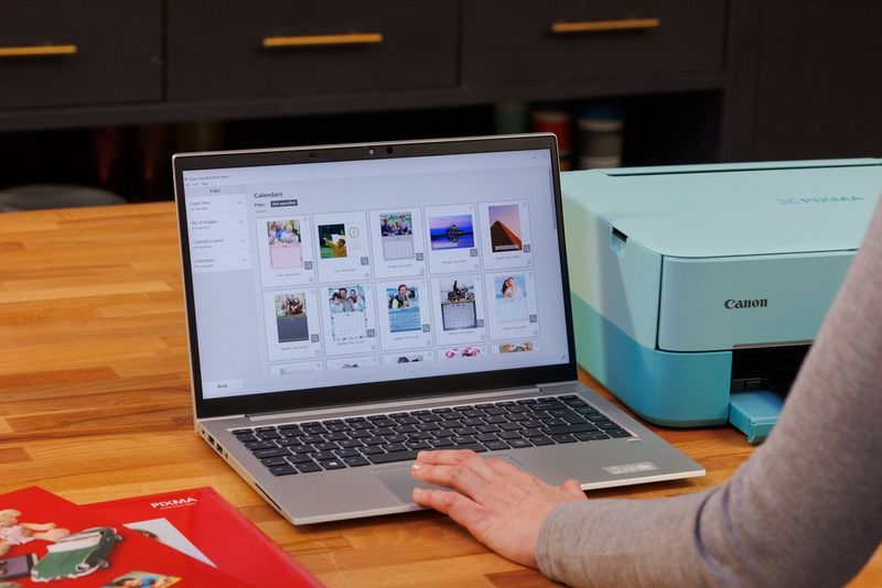 A laptop on a wood-effect desk alongside a Canon PIXMA printer.