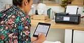A woman with her back to the camera uses a tablet. A Canon printer is on a desk in the background.