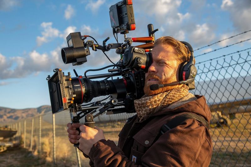 A man wearing headphones and warm clothes filming outside with a Canon EOS C300 Mark III on his shoulder. 