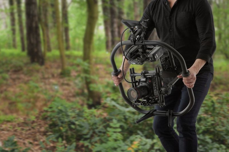 A man holding an EOS C500 Mark II on a gimbal, filming in a forest. 