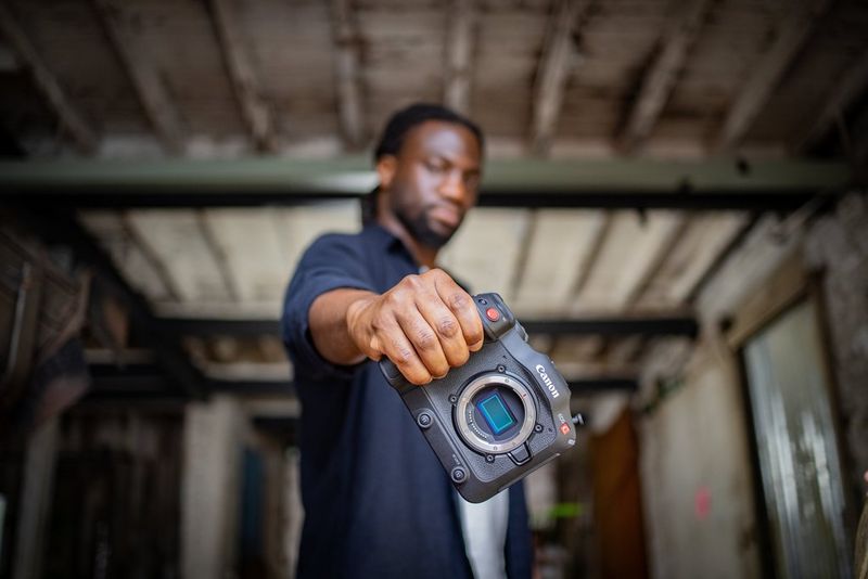 A man with his arm outstretched holds a Canon EOS C70 camera with no lens attached.